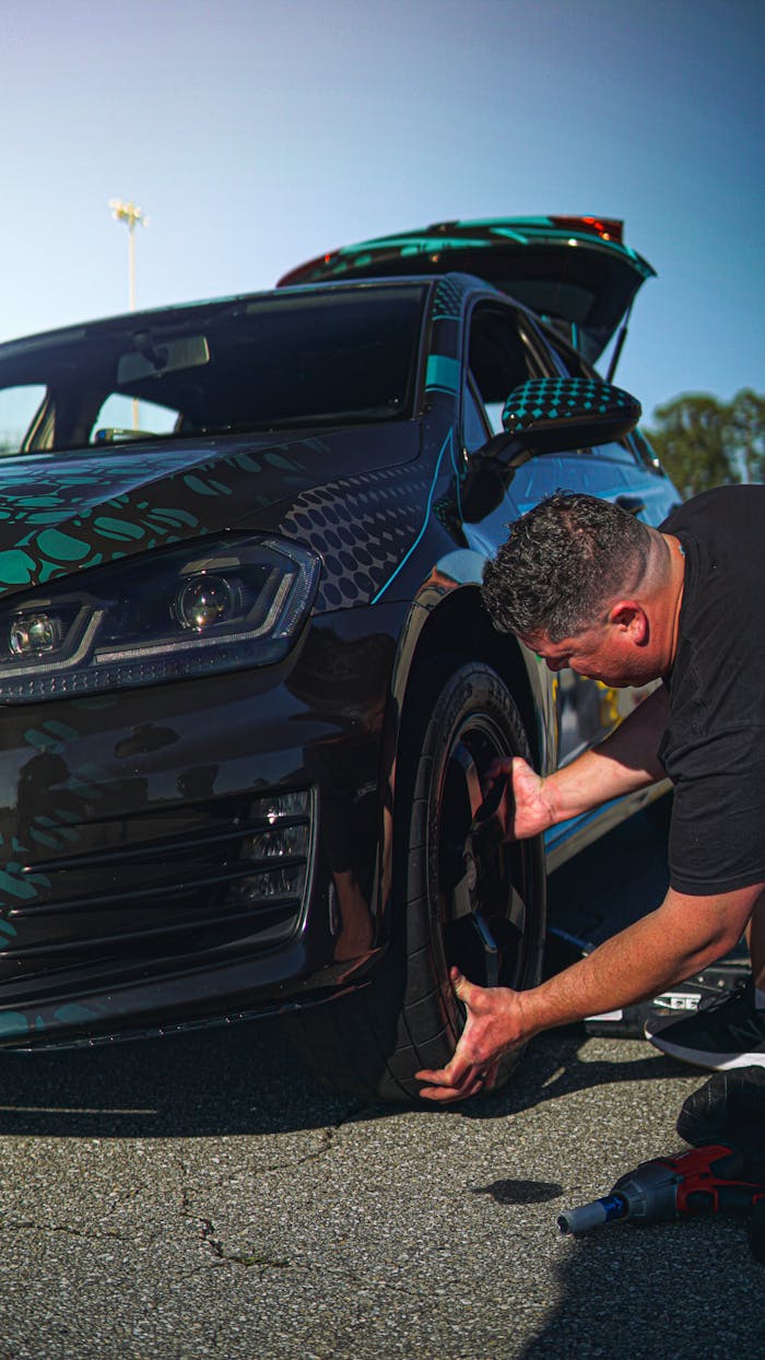heros-img Expert mechanic changing tire on sleek black sports car under clear sky.