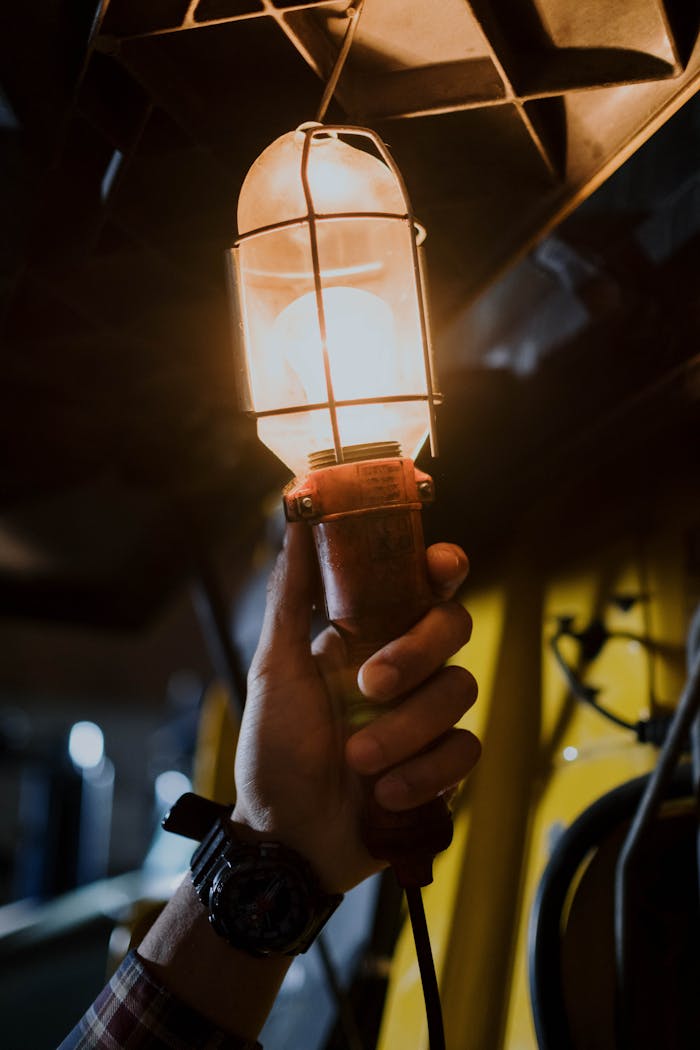 about-us A hand holds a vintage garage work light, illuminating a dark space.